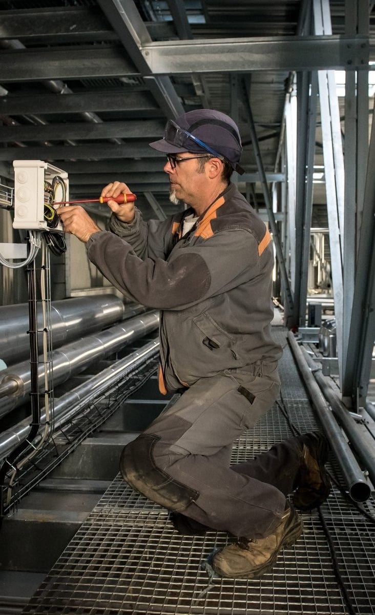 Portrait d'un technicien réparant un circuit électrique lors d'un reportage métier.